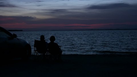 Silhouettes of a couple sitting at the beach watching the red sky from the sunset