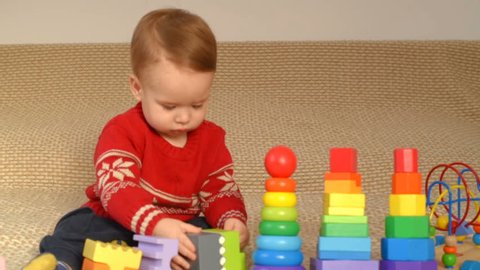 
Cute little kid boy playing with lots colorful wooden blocks toy at home.Toddler boy play with toys. Adorable little boy playing with colorful cubes. Happy child playing colorful blocks.