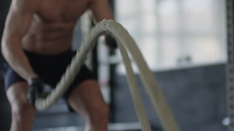 Mid-section of unrecognizable shirtless sportsman working out with rope during cross-training routine