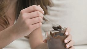 Satisfied young woman eating melted chocolate with spoon from a jar at home