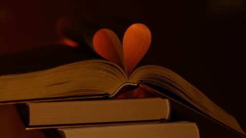 A stack of books with an open book on top. Creation the heart from book sheets. Heart made of sheets of the book is highlighted