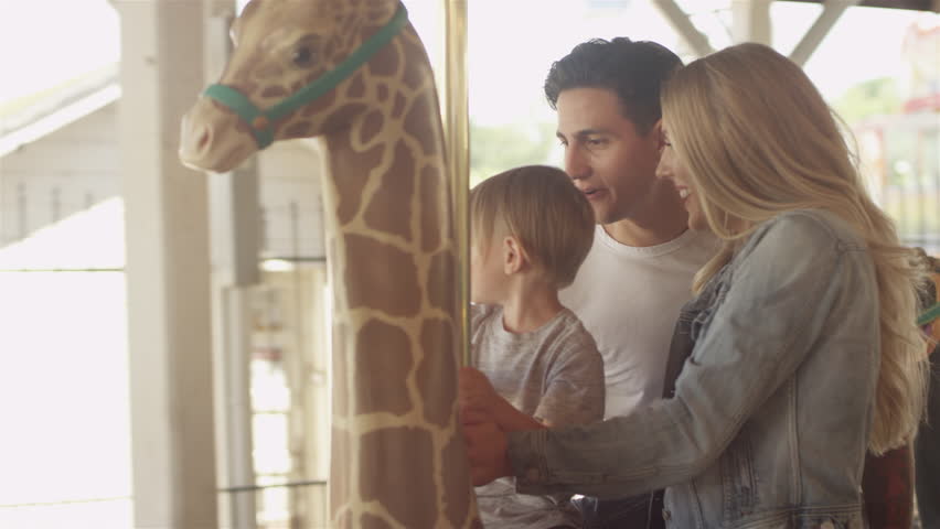 Loving family smiling at each other, while riding a carousel at an amusement park