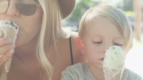 Little kid accidentally shoves an ice cream cone on his face, and laughs out loud with his mother at the park