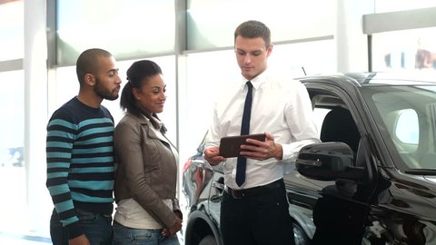 Explaining the Characteristics. Young Handsome Car Seller Using a Digital Tablet to Explain Something to His Customers at the Local Car Dealership