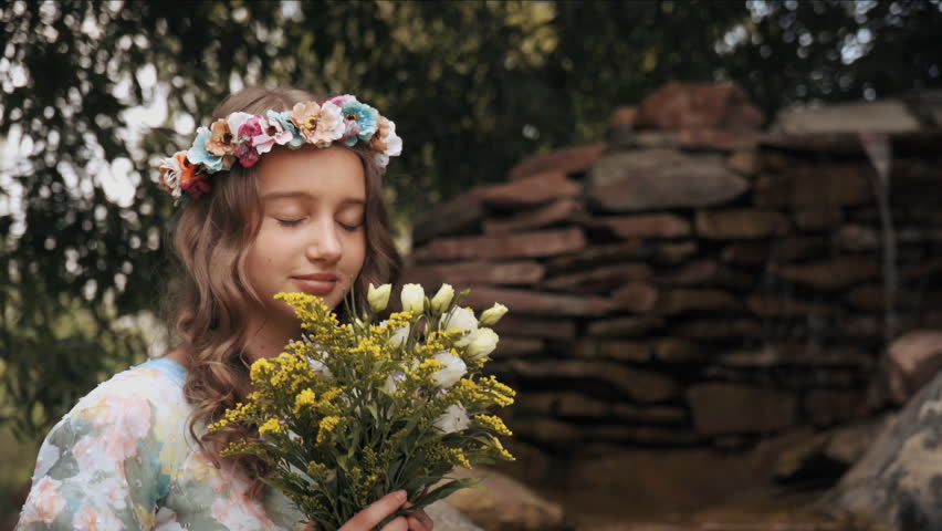 A pretty young girl sniffing a bouquet of flowers in the park near waterfall. In slow motion mode.  