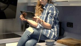 Girl sits on worktop in the kitchen and watches video on tablet, steadycam shot
