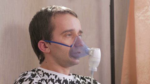 Young man holding a mask from an inhaler at home. Treats inflammation of the airways via nebulizer. Preventing asthma and cough