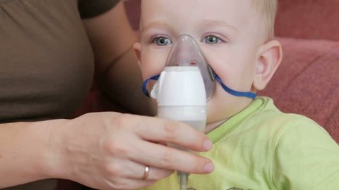 Mother holds the mask on the baby inhaler and breathes the medicine at home. Treats inflammation of the airways via nebulizer. Preventing asthma and cough