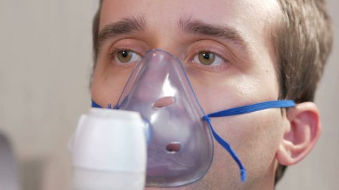 Young man holding a mask from an inhaler at home. Treats inflammation of the airways via nebulizer. Preventing asthma and cough