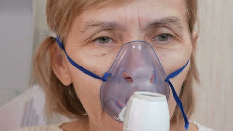 Senior woman holding a mask from an inhaler at home. Treats inflammation of the airways via nebulizer. Preventing asthma and cough