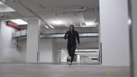 Young Man Sprinting Past Camera in Car Park in Slow Motion Dolly Shot
