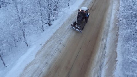 tractor rides on a snowy road in the forest, aerial view