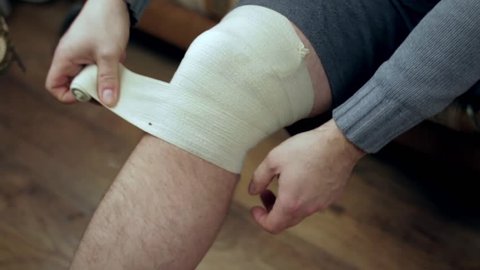 Young man wrapping his knee injury with elastic bandage closeup