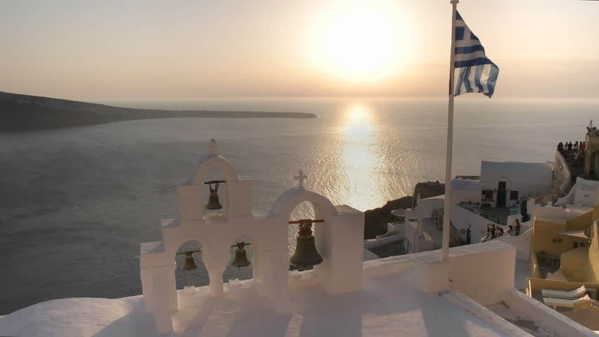 greek flag and four bells at sunset in oia on the island of santorini, greece