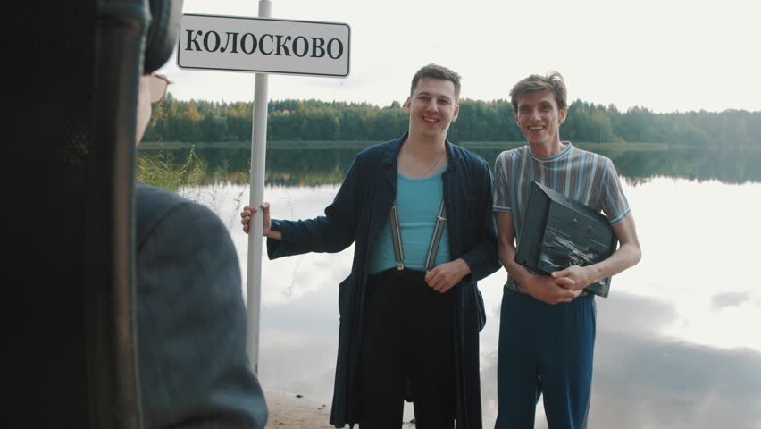 Two men stand on lake shore with city sign and monitor tablet talking to businessman on a summer day