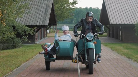 Biker with tie ride motorcycle with woman in nurse costume grimacing in sidecar