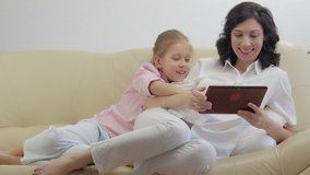 Mother with daughter using tablet computer, laughing and looking in digital tablet.