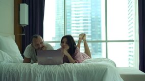 Young, happy couple watching movie on laptop lying on bed at home
