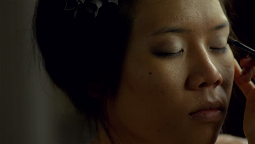 Makeup artist applying eyeshadow to the eyelids of an Asian woman.