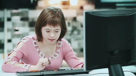 Girl with Down syndrome sitting at a computer at home and typing text.