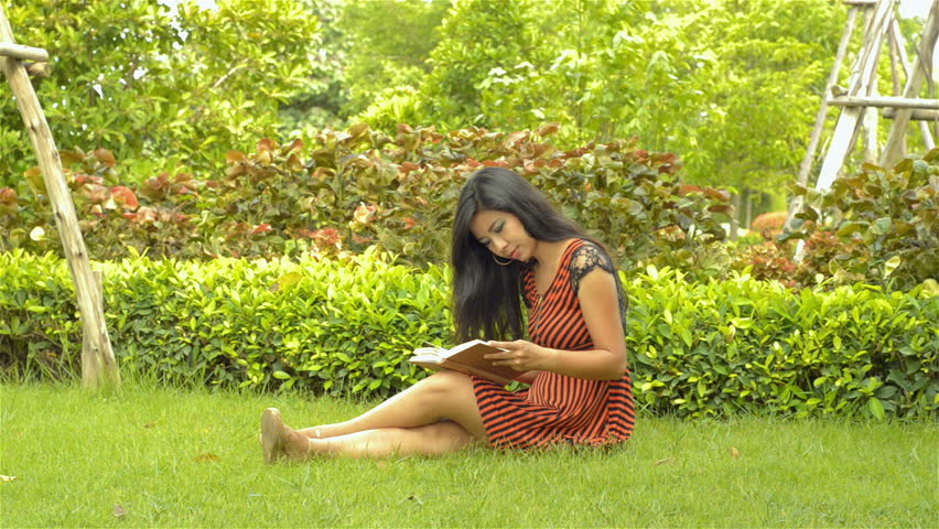 A beautiful young Asian woman reading a book, while relaxing, sitting on the