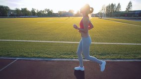 Slow motion. Beautiful young woman exercise jogging and running on athletic track on stadium at sunrise. Cinematic style video.