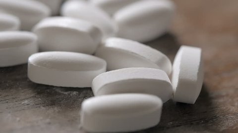 White prescription pills fall into a  large pile in slow motion. 
