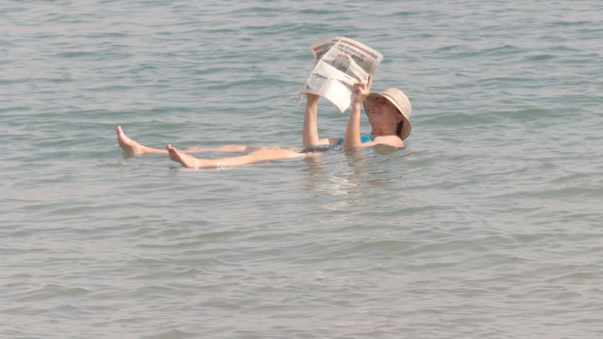 a woman reads a newspaper while floating in israel