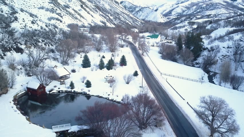 UTAH COUNTY, UTAH - FEB 2017: Aerial mountain valley winter snow cabin on pond. Winter snow landscape. Pond, stream and cabin. Mountain valley landscape. Cold season weather. Nature and environment.