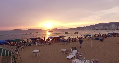 4K aerial of a busy beach in Acapulco flying over the ocean during a beautiful sunset