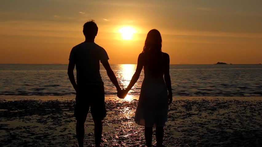 Couple silhouette staring at sunset on the beach start kissing and she lifts one leg up bending her knee in Koh Phangan island, Thailand. Valentine Day, honeymoon romantic love celebration concept