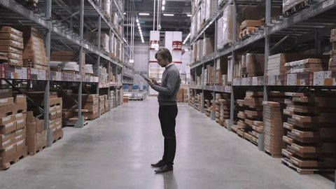 Manager With Tablet PC Checking Goods At Supermarket Warehouse. Modern Furniture Stock