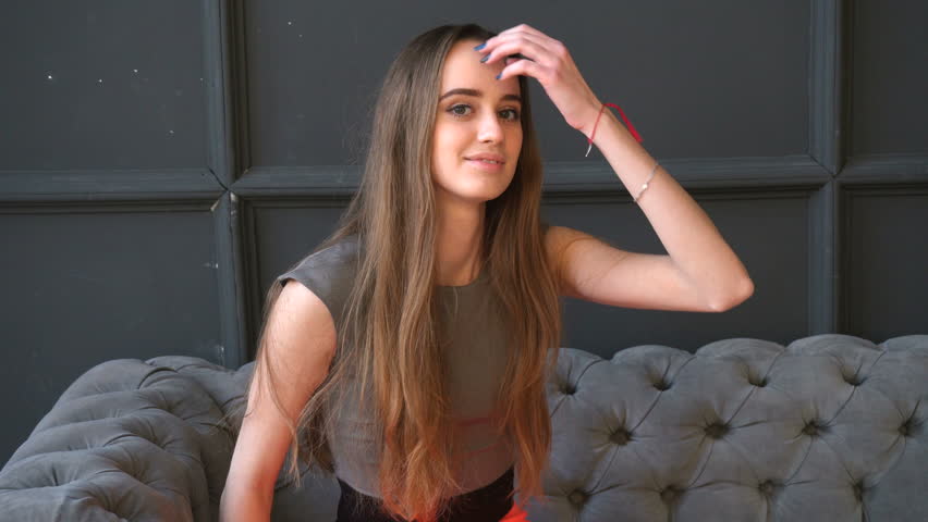 Beautiful girl in dress is sitting on the soft gray couch