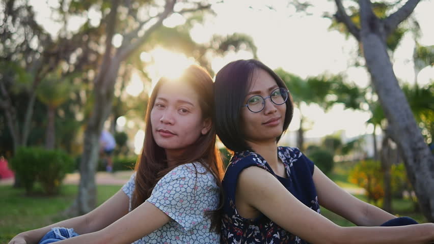 Woman waving hands saying hello in public park. Smiling happy girl having fun. Asian model lookin at camera.