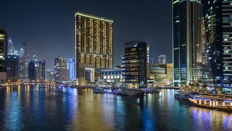 Night timelapse of Dubai Marina with floating yachts in harbor and modern towers. Glittering lights and tallest skyscrapers during a clear evening with Blue sky. 4K 