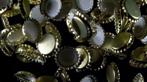 Thrown Beer Lids. Golden beer bottle caps floating in the air on a black background. Slow Motion at a rate of 240 fps