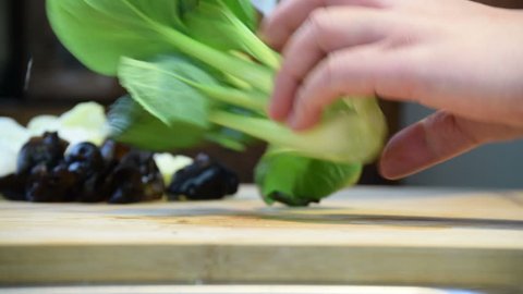 Close-up of professional chef's hands slicing, preparing pak choi, bok choy in half for cooking