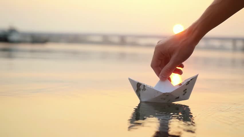 Man's hand launches paper boat on the water and pushing it away during beautiful sunset with reflection sun in the sea in slowmotion. 1920x1080