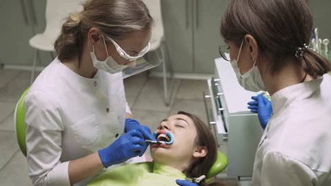 Dentists produce teeth cleaning girl, using tools. 4k footage. Dental clinic. Close-up.