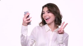 Smiling cute woman making selfie photo on smartphone and waving to camera isolated on a white background