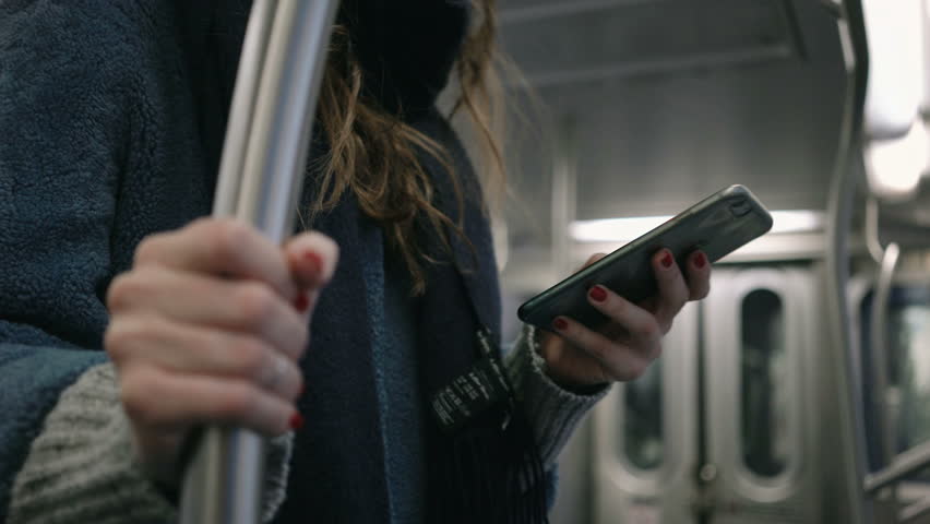 Woman in warm clothes and eyeglasses using smartphone in metro train