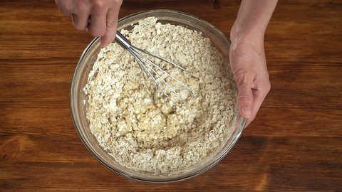 Woman make dough for oatmeal cookies in glass bowl, top view slow motion video