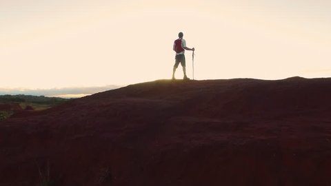 4k drone footage of hiker walking  and looking at view with red backpack in desert mountain terrain at sunset. 