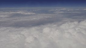 White compact clouds, horizon line and blue sky from airplane window, mobile phone video.