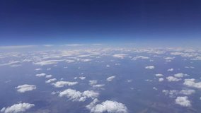 Blue sky below clouds from window of flying airplane, mobile phone video.