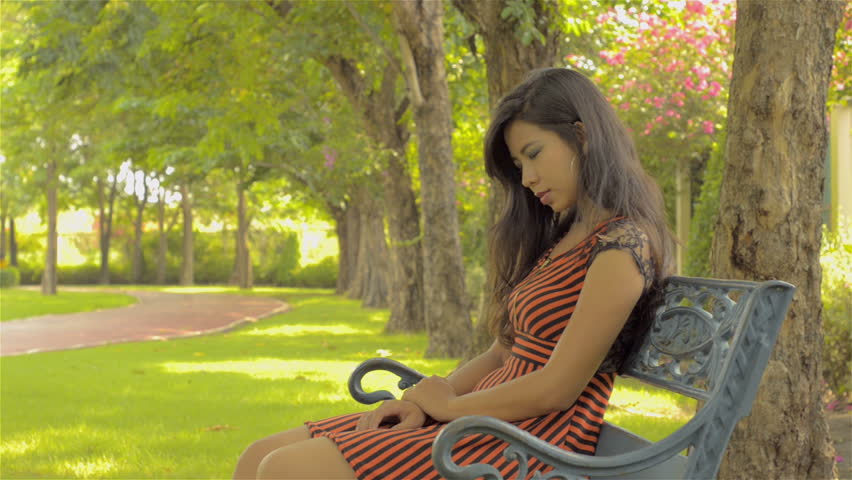 A young Asian woman sitting on a park bench, praying earnestly.