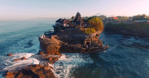 Pura Tanah Lot temple on a rocky island. A cultural symbol of Indonesia. Classic oriental temple and ocean. Sunlight. Aerial view. Bali, Indonesia