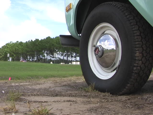 A chrome hubcap on a vintage 4 wheel drive vehicle in the foreground.