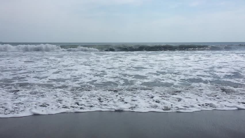 Surf from blue ocean waves lapping over empty sandy beach slow motion