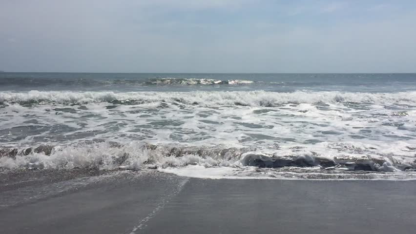 Surf from blue ocean waves lapping over empty sandy beach slow motion